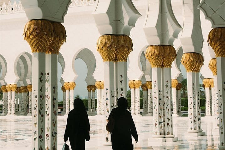 Visitors walking beneath the gold-topped columns inside Sheikh Zayed Grand Mosque