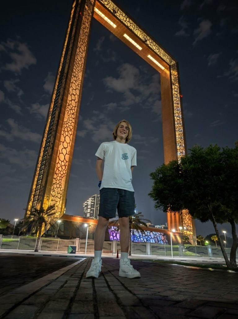 Traveller standing beneath the golden lattice of the Dubai Frame at dusk