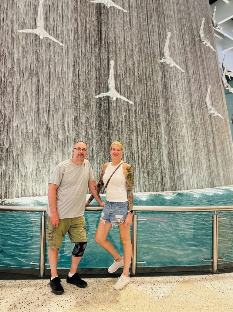Couple smiling in front of the Dubai Mall waterfall with its diving sculptures